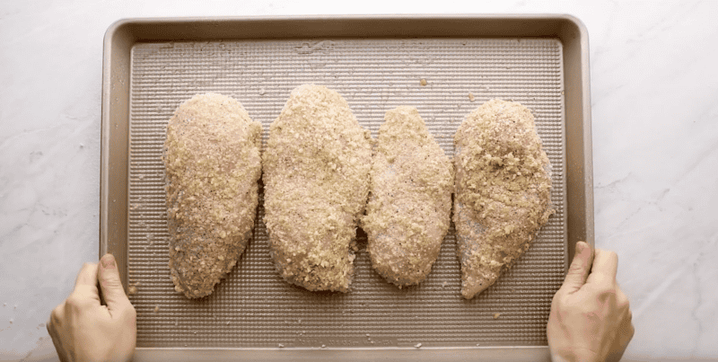 4 panko-breaded chicken breasts on a baking sheet.