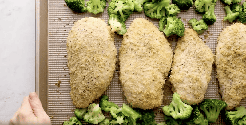 baked panko-coated chicken breasts on a baking sheet with frozen broccoli.