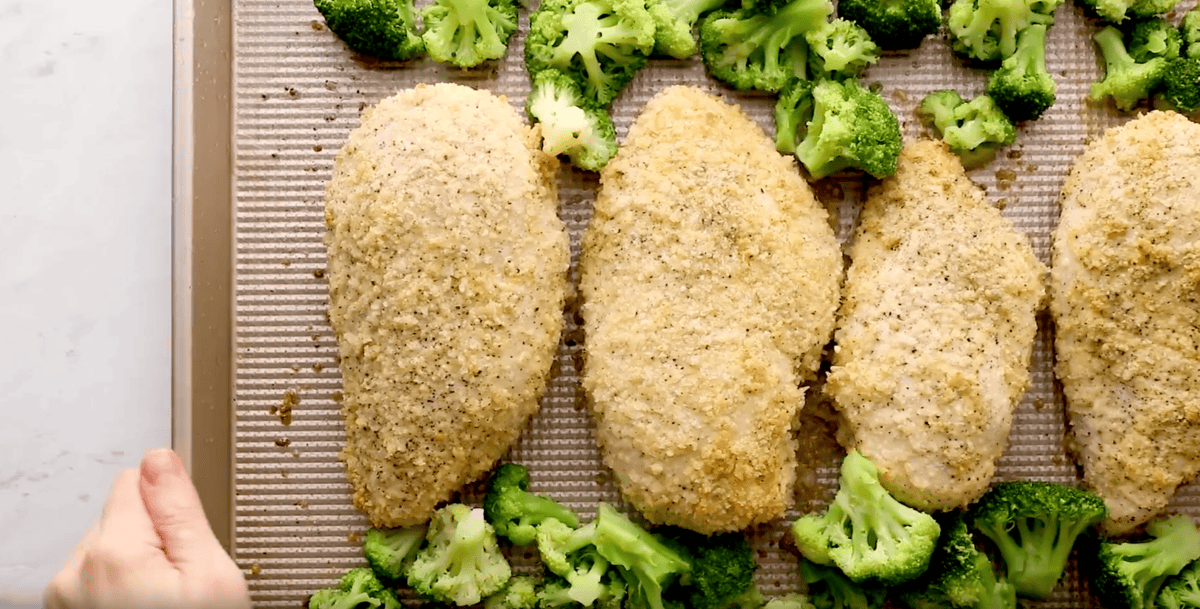 baked panko-coated chicken breasts on a baking sheet with frozen broccoli.