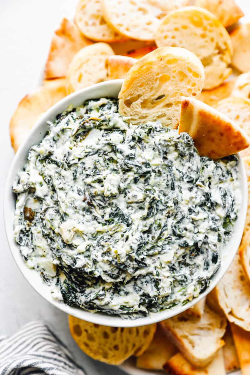 crockpot spinach dip in a white bowl with dippers