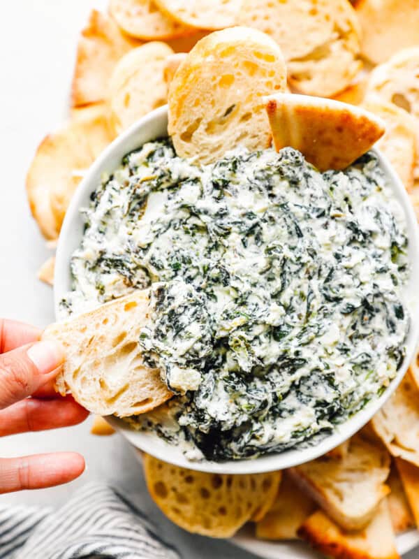 crockpot spinach dip in a white bowl with dippers