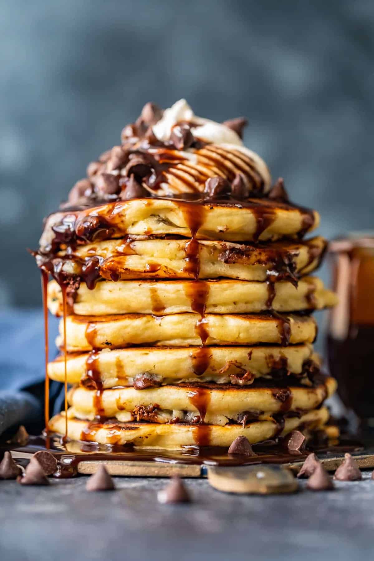 lots of chocolate chip pancakes stacked on each other drizzled with chocolate syrup and whipped cream