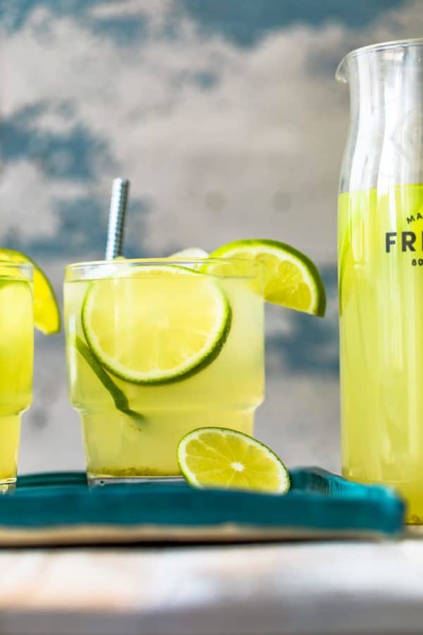 a pitcher of lemonade with limeade and lime slices next to it.