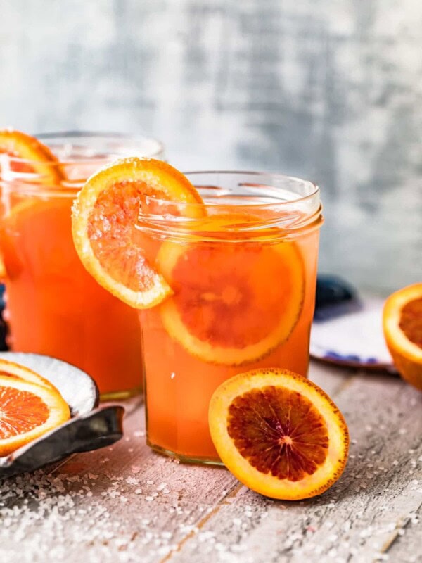 blood orange paloma in glass garnished with oranges