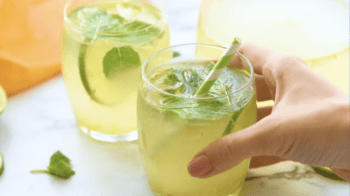 holding a glass of limeade with ice, mint, lime slices, and a straw.