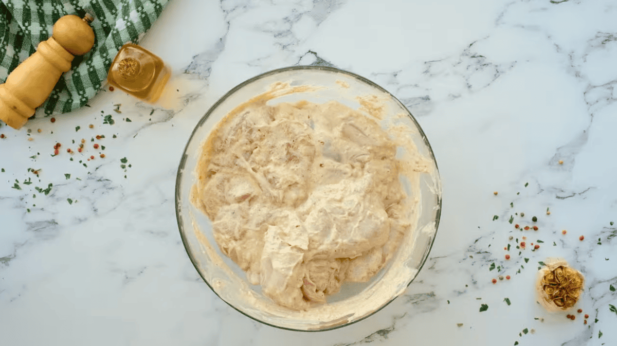 chicken thighs coated in seasoned yogurt in a glass bowl.