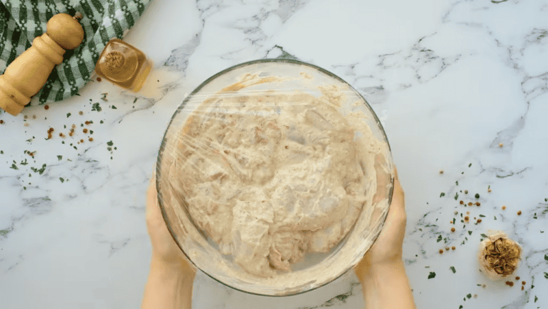 a bowl full of yogurt marinated chicken thighs covered with plastic wrap.