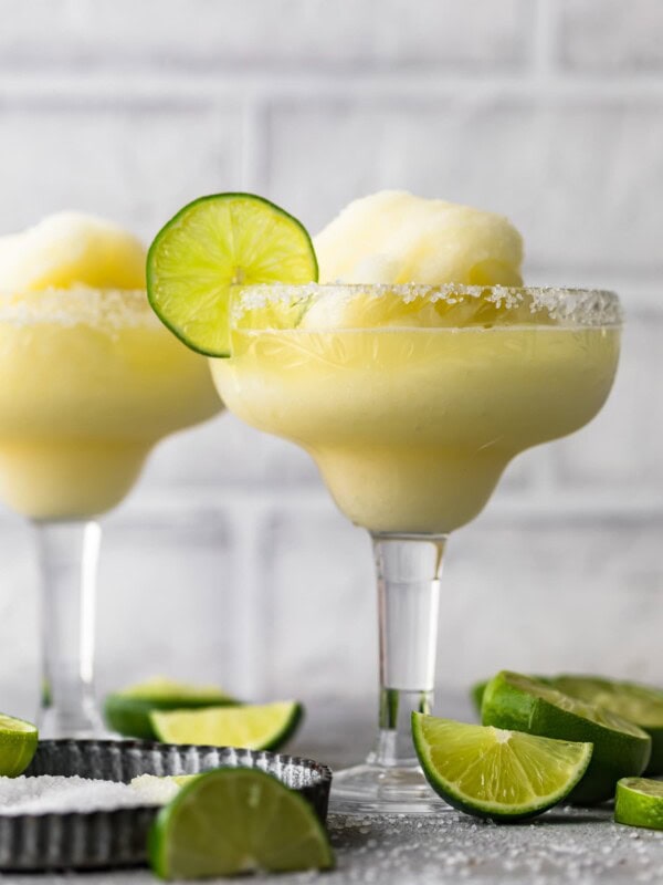 two frozen margarita glasses surrounded by sliced limes