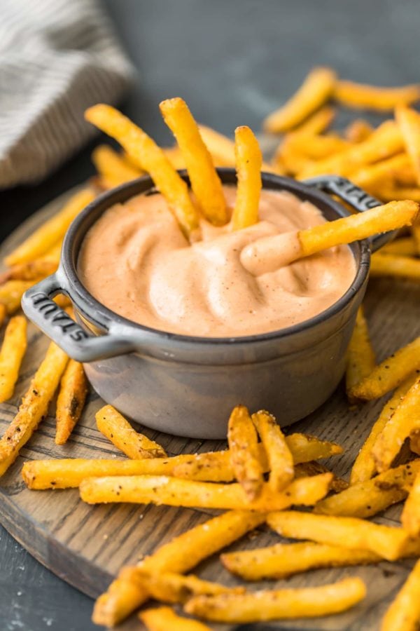 A bowl of fry sauce with french fries on a wooden cutting board.