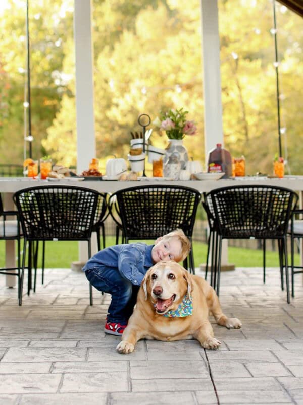 A young boy hugging a dog with a table behind them