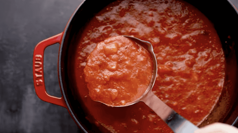 a ladleful of marinara sauce over a dutch oven.