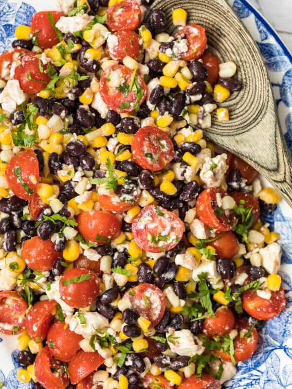 tomato corn salad on platter with wooden spoon