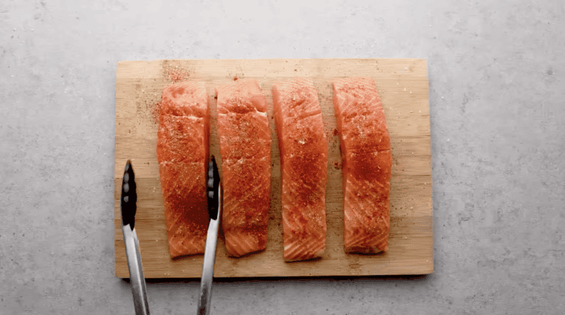 4 seasoned salmon fillets on a cutting board.