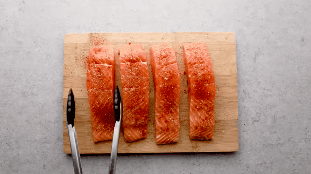 4 seasoned salmon fillets on a cutting board.