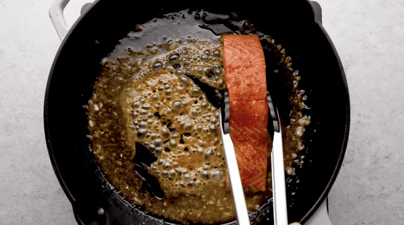 adding seasoned salmon fillets to sauce in a pan.