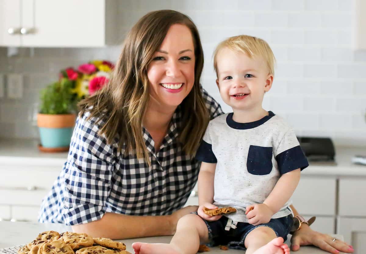 A food blogger posing with her baby in front of a kitchen counter.