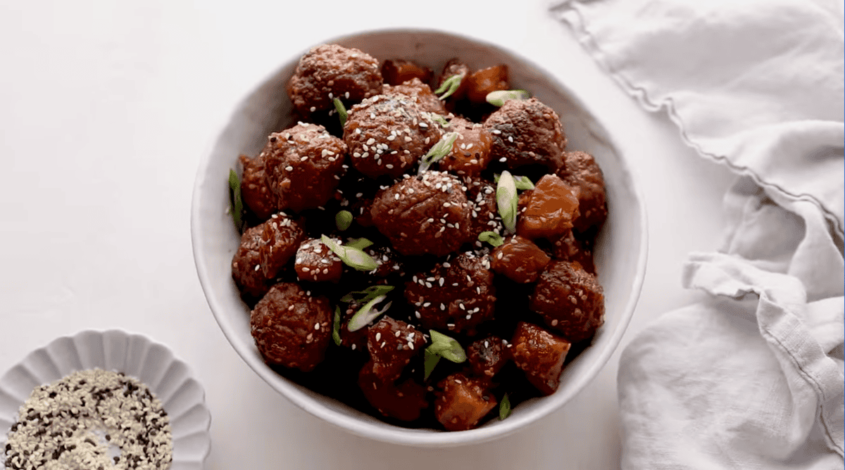 crockpot teriyaki meatballs in a white bowl topped with sesame seeds and green onions.