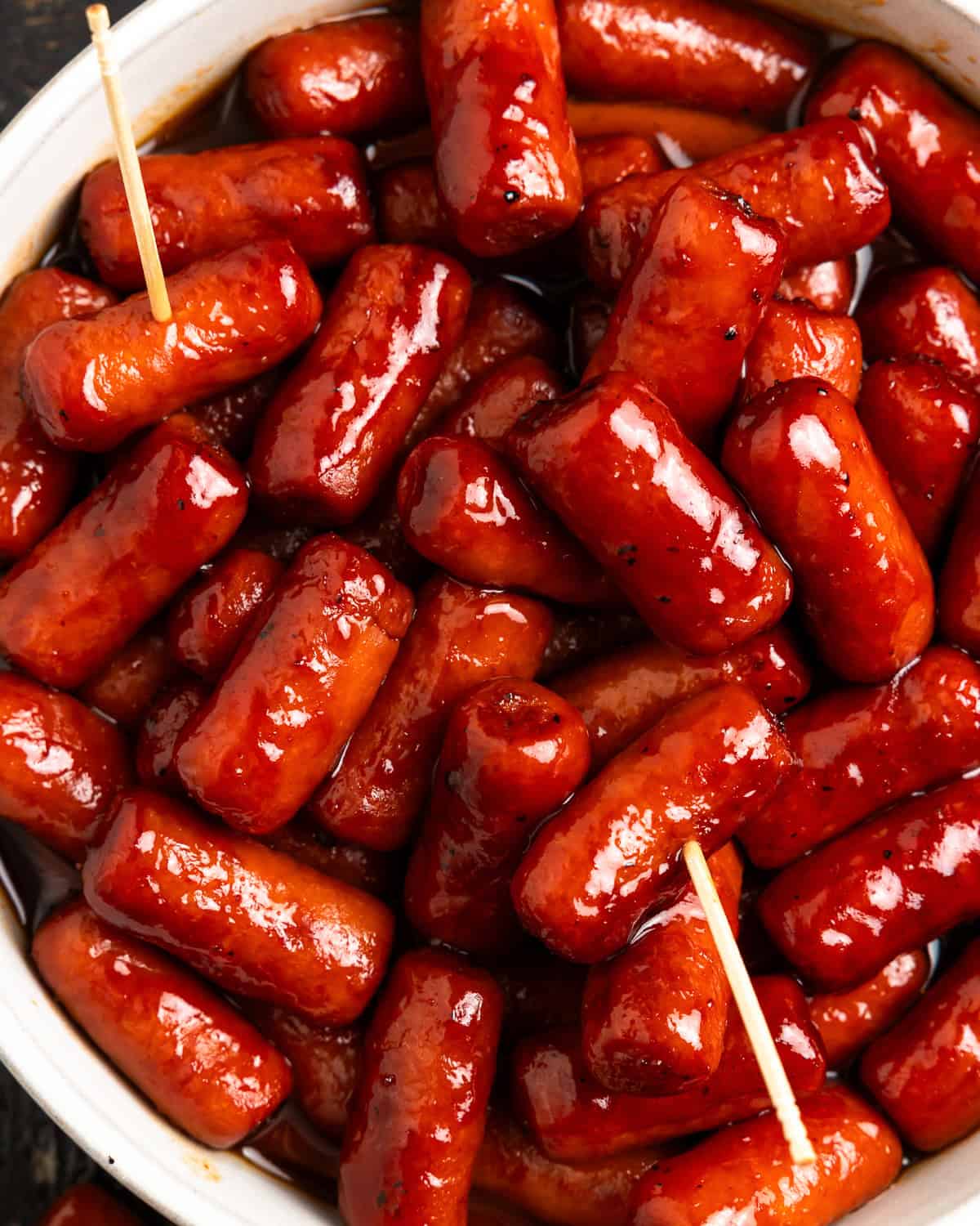 overhead view of little smokies in a white bowl with toothpicks.