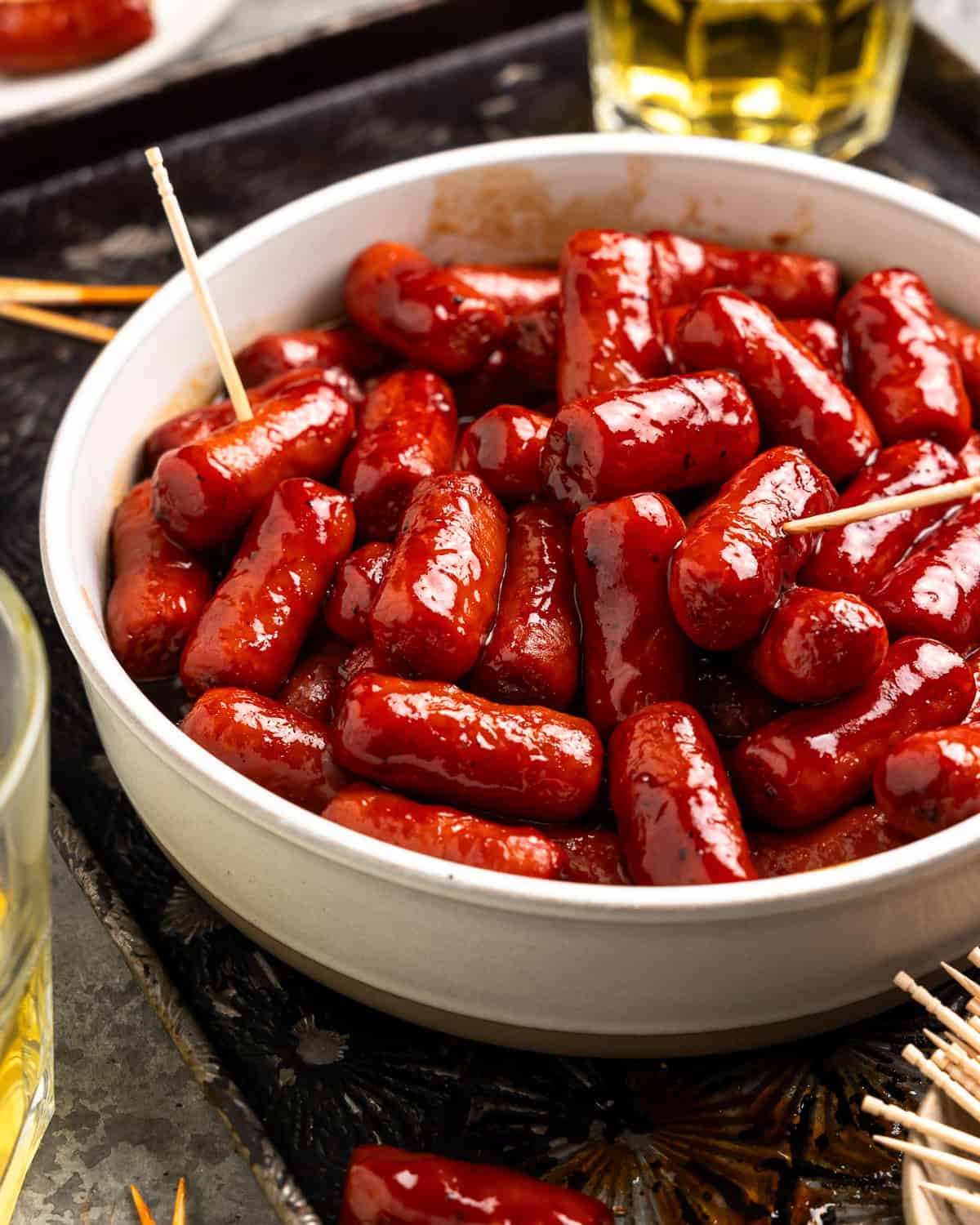 little smokies sausages in a white bowl with toothpicks.