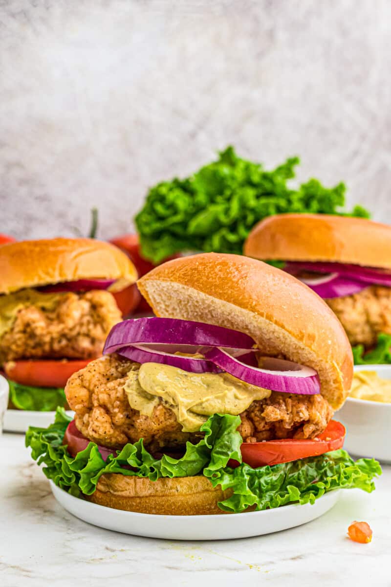 crispy chicken sandwiches with lettuce tomato and onion. topped with dijon mustard.