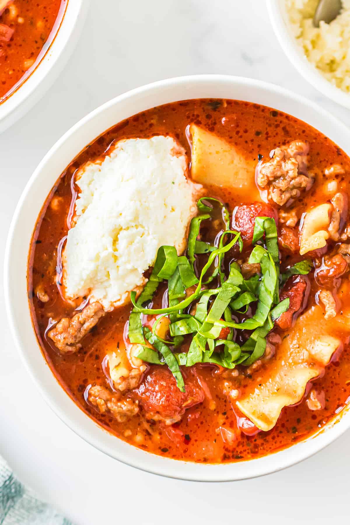 up close lasagna soup garnished with ricotta and basil