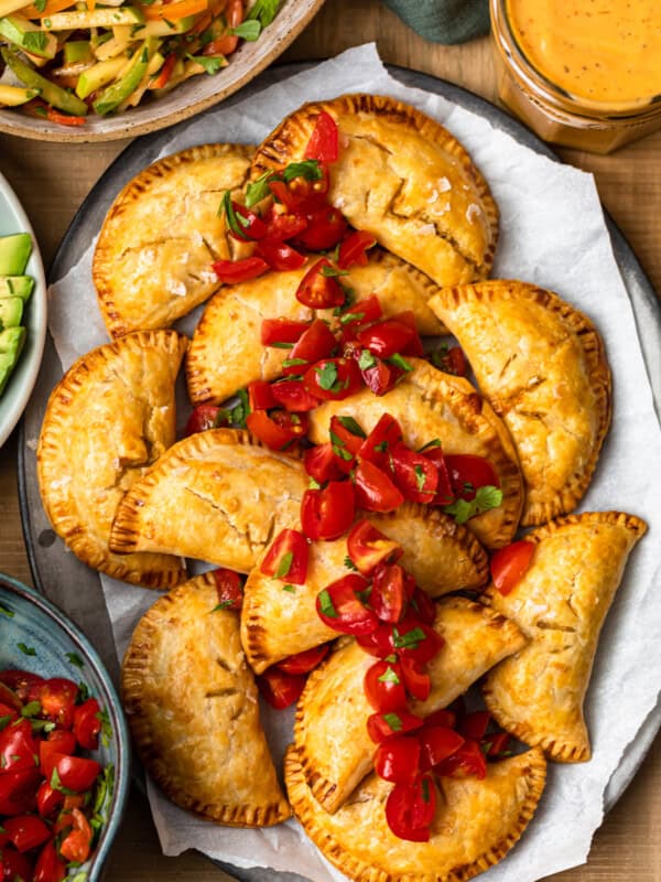 overhead baked chicken empanadas on platter garnished with tomatoes