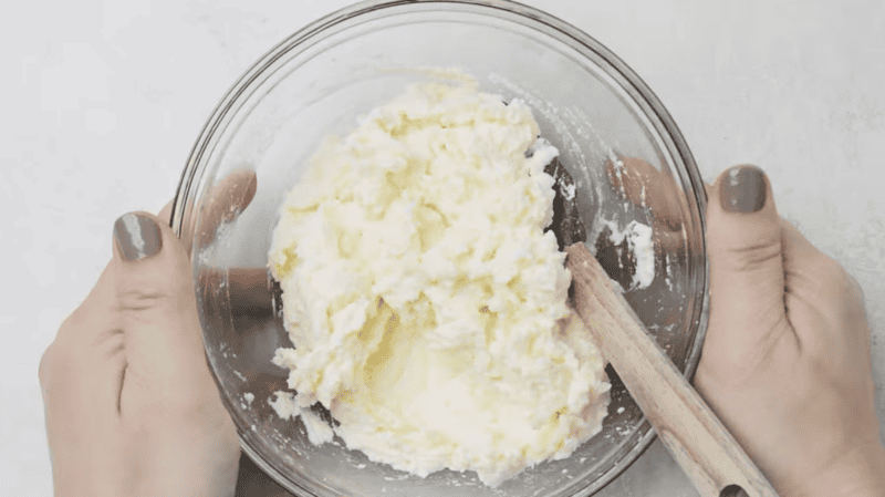 mixed ricotta and mozzarella cheese in a glass bowl with a rubber spatula.