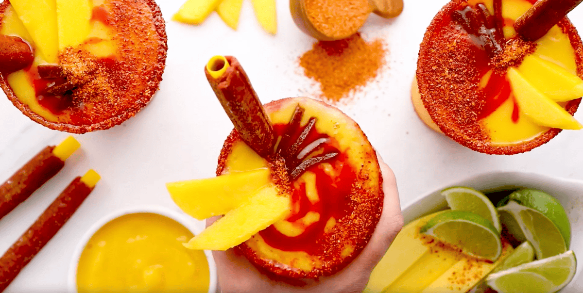 overhead view of mangonadas topped with chamoy, mango slices, tamarind lollipops, and pulparindo candies.