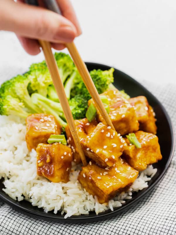 chopsticks grabbing a cube of air fryer teriyaki tofu on a black plate.