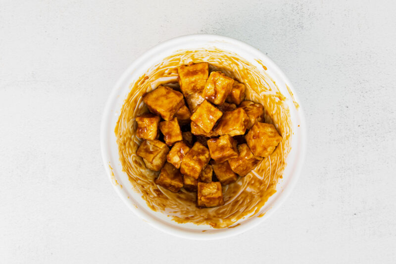 cubes of air fryer teriyaki tofu coated in sauce in a white bowl.