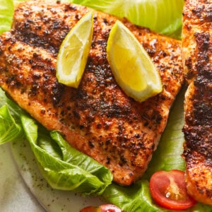 overhead view of an air fryer salmon filet on a bed of lettuce topped with lime wedges.