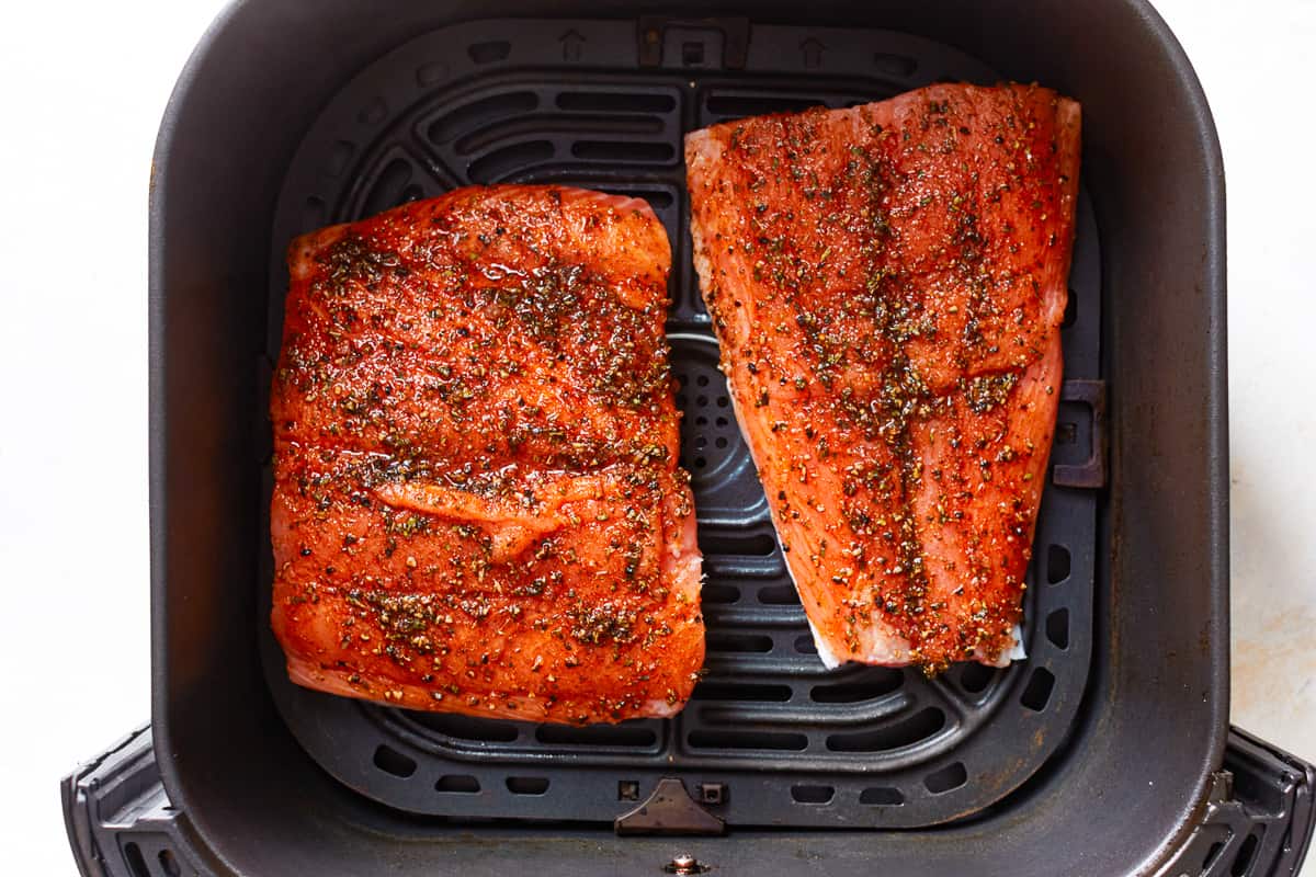 2 seasoned salmon filets in the basket of an air fryer.