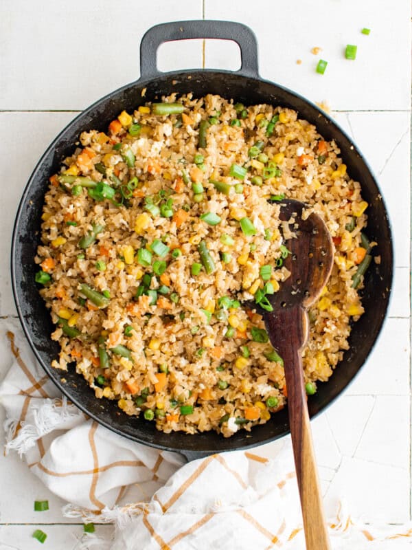 overhead view of cauliflower fried rice in a cast iron pan with a wooden spoon.