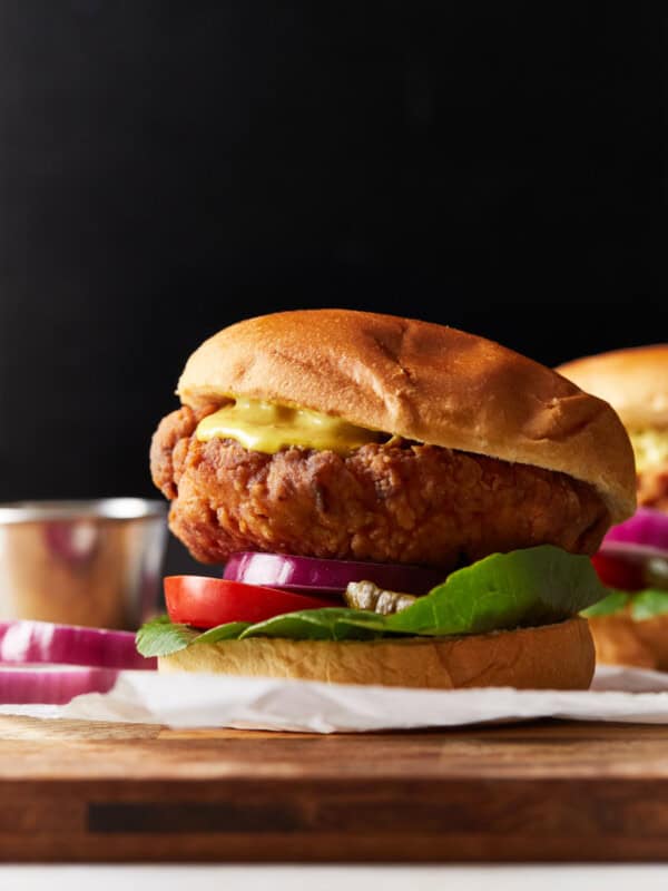 side view of a crispy chicken sandwich on a wooden cutting board.