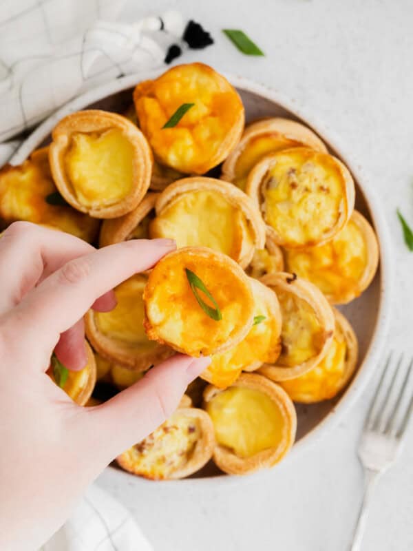 hand grabbing a mini quiche from a white plate of mini quiches.