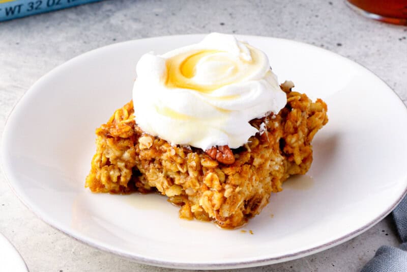 slice of pumpkin pie baked oatmeal with whipped cream and maple syrup.