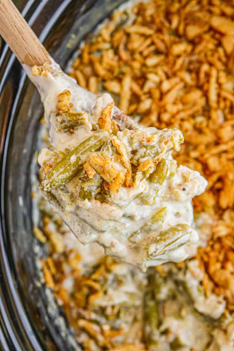 holding wooden spoon up with crockpot green bean casserole