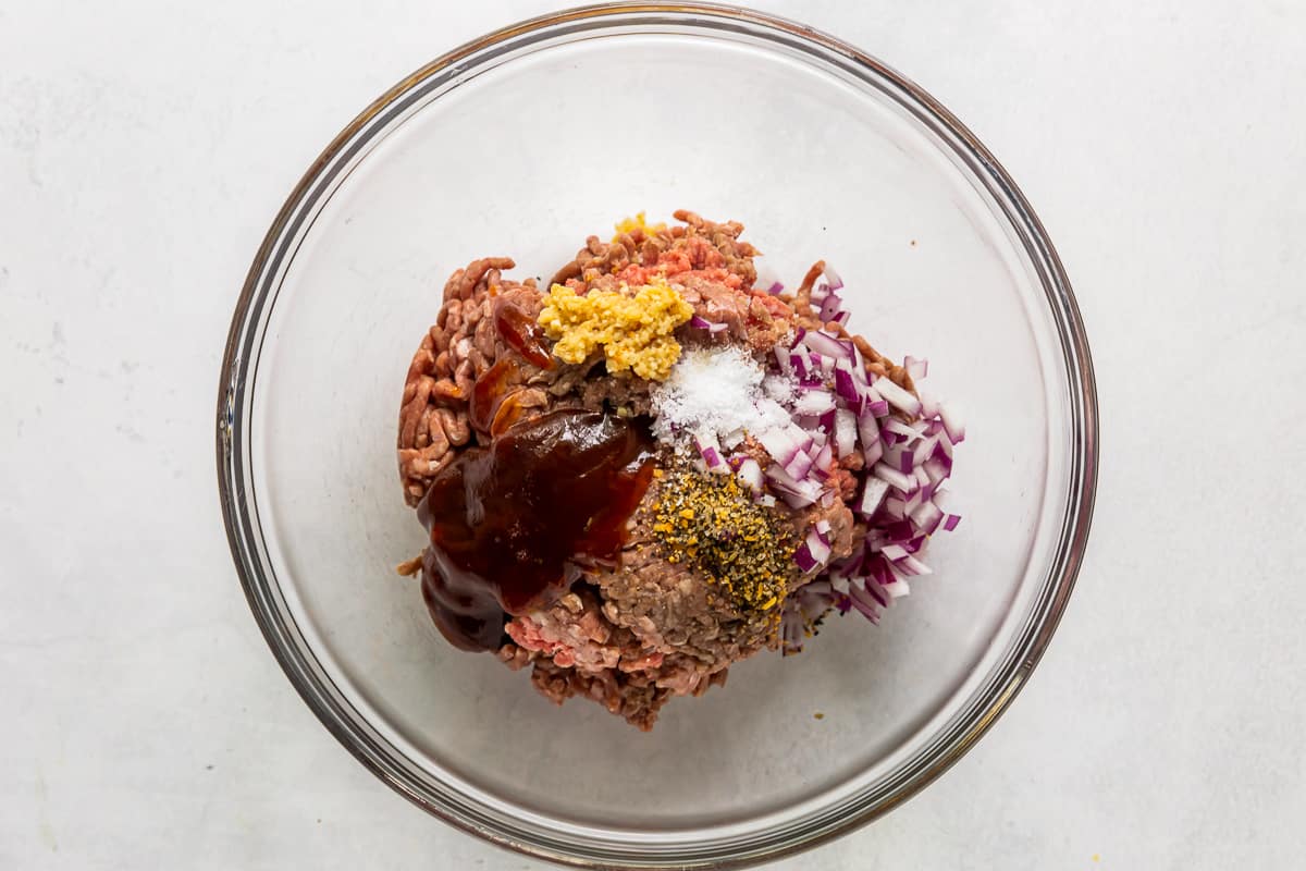 hamburger meat, onion, garlic, spices, and bbq sauce in a glass bowl.