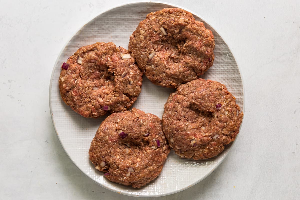 4 dimpled burger patties on a plate.