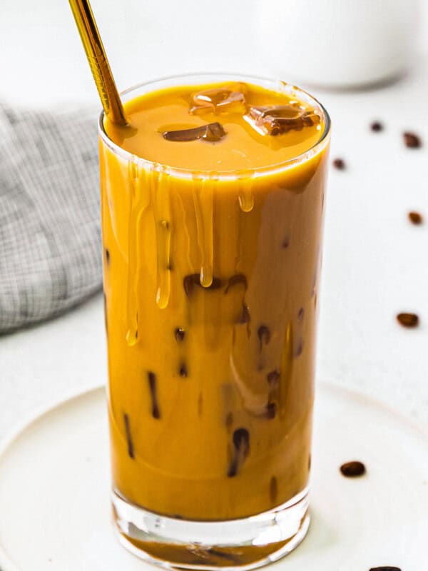 up close stirred iced caramel latte in glass with gold straw