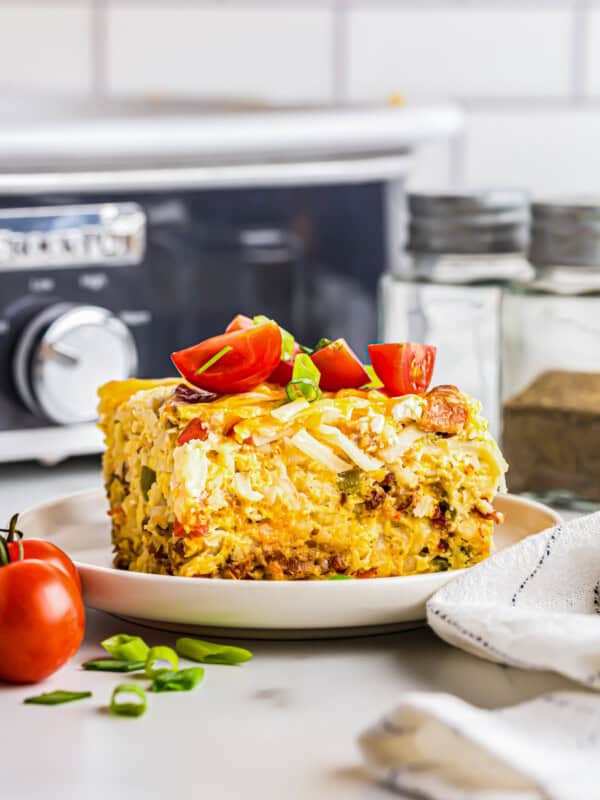 slice of breakfast casserole topped with diced tomatoes on a white plate