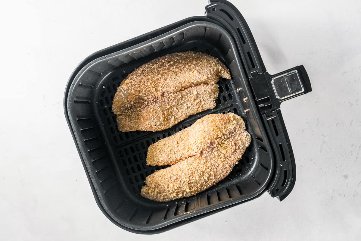 2 breaded tilapia filets in air fryer before cooking