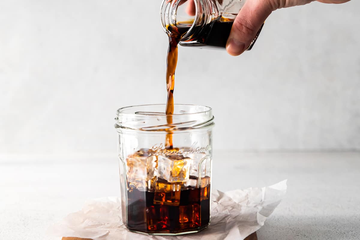 hand pouring espresso into clear glass filled with ice