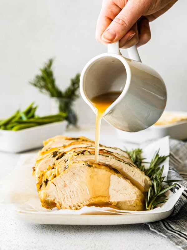 hand pouring gravy onto slices of garlic herb turkey breast