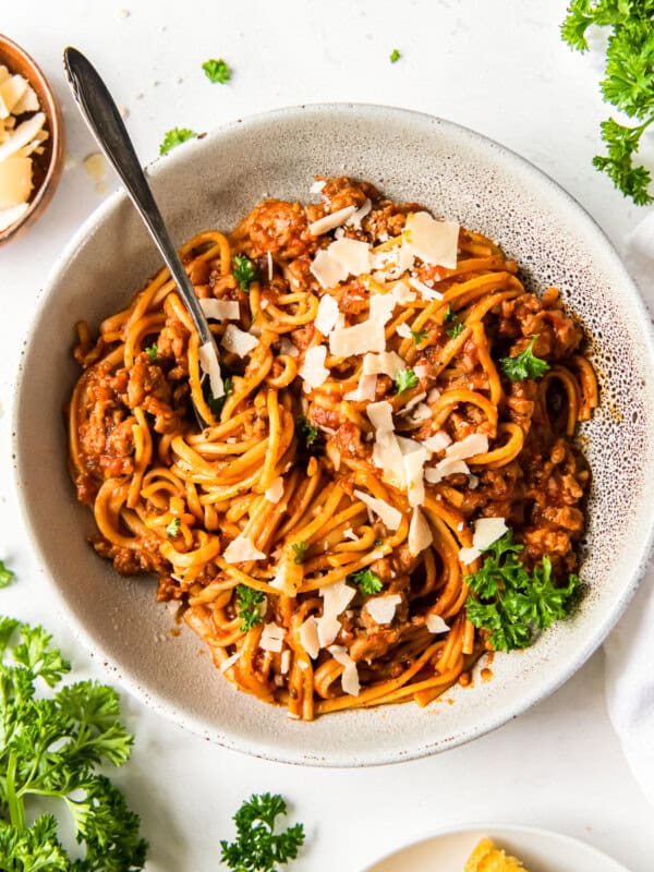 spaghetti topped with herbs and parmesan cheese in a white bowl with a fork