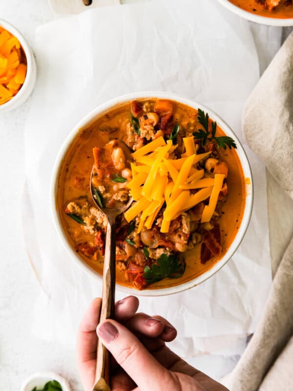 hand holding a spoon in a bowl of turkey white bean chili