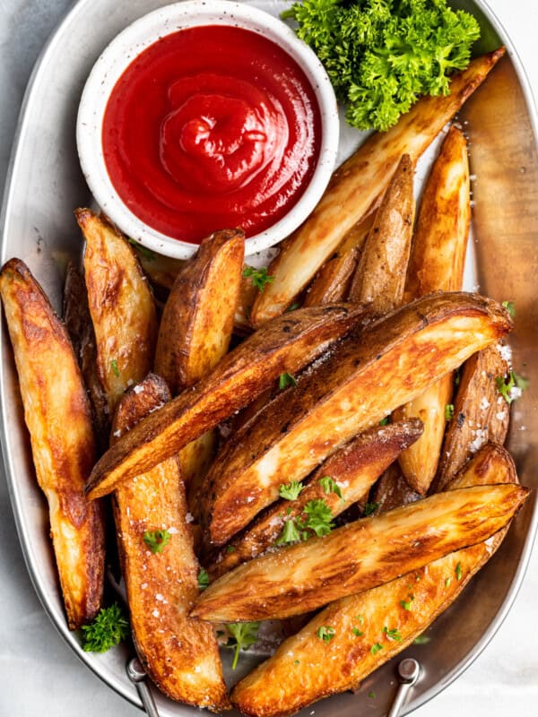 potato wedges on a white serving platter with ketchup in a white bowl