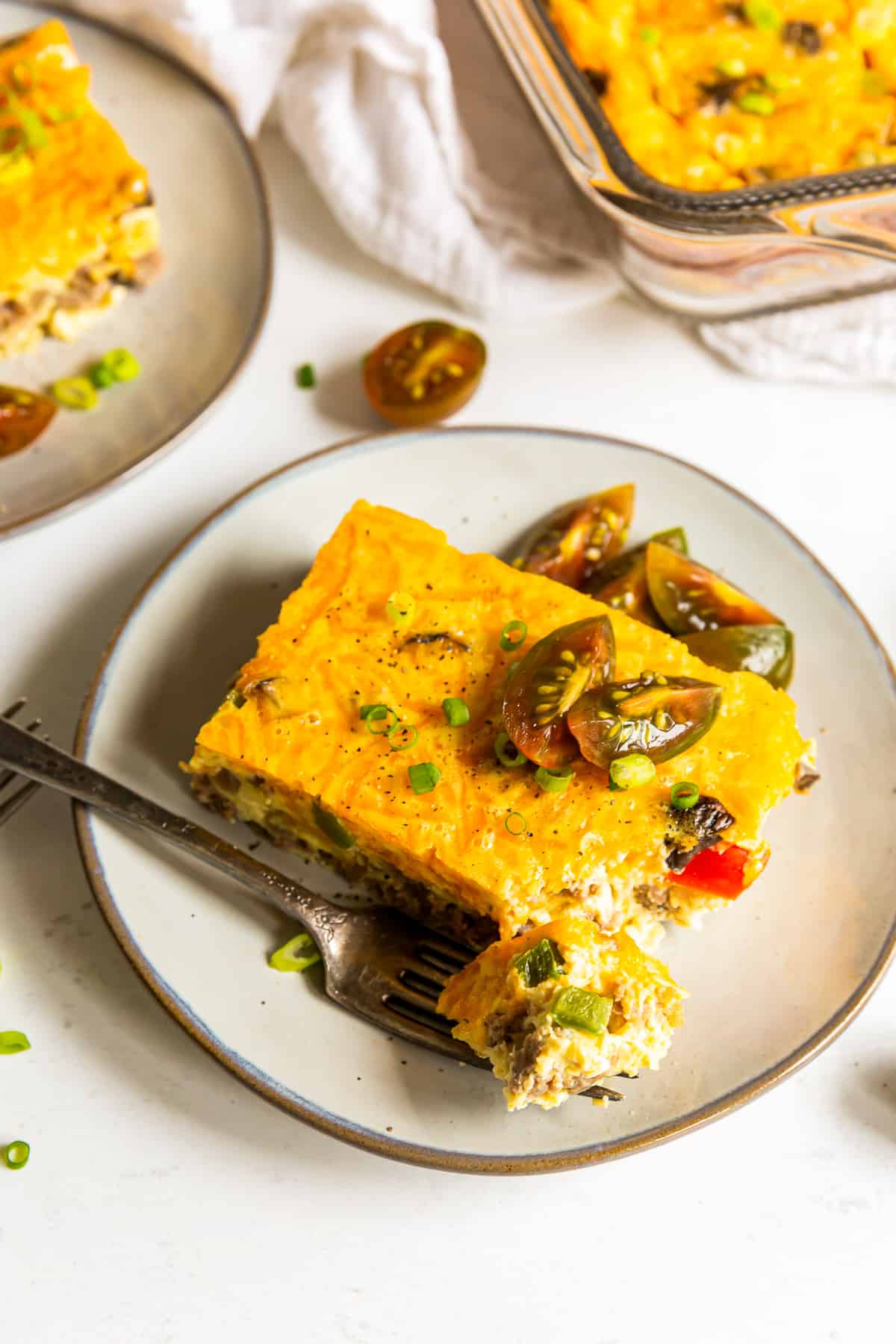 piece of sausage breakfast casserole topped with fresh tomatoes on a white plate with a fork