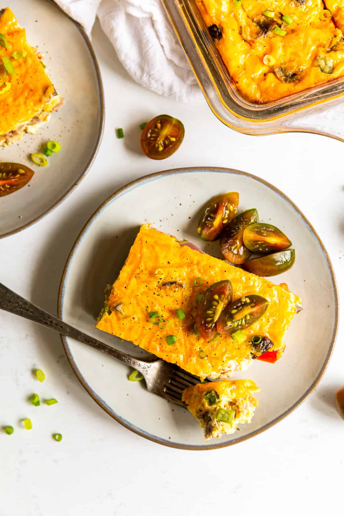 piece of sausage breakfast casserole topped with fresh tomatoes on a white plate with a fork