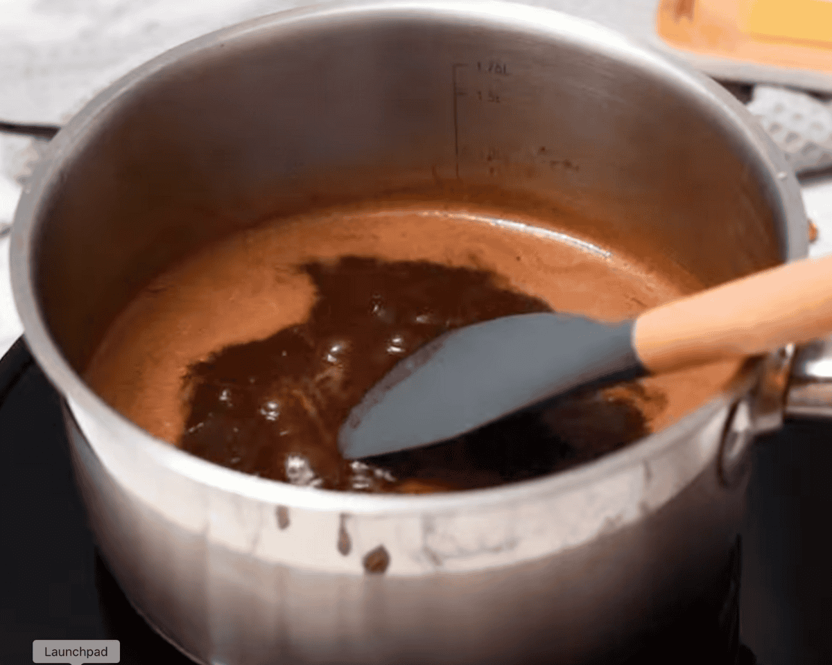 A saucepan on the stove with a bubbling chocolate mixture being stirred with a silicone spatula.